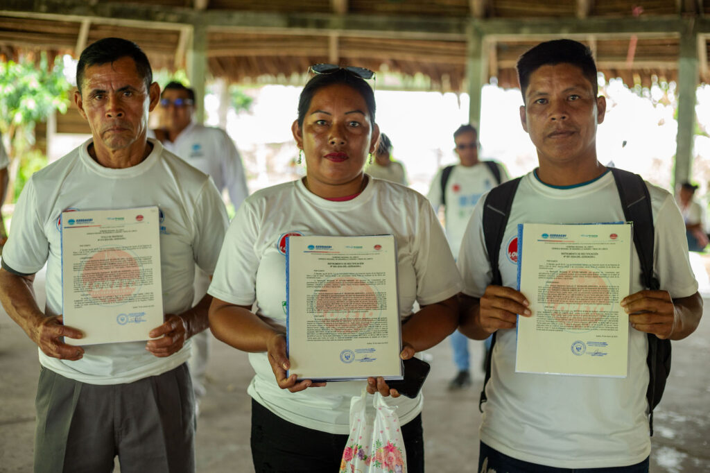 Three Indigenous leaders hold their land titles and smile for the camera