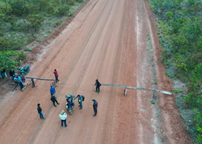 Indigenous community members set up a wooden blockade across a dirt road leading into their territory. 