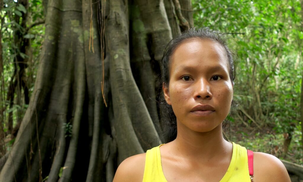 Jhuliana Sebastian Gomez, the first female leader of the Ticuna community San Francisco de Yahuma stands in front of an ancient tree in her territory
