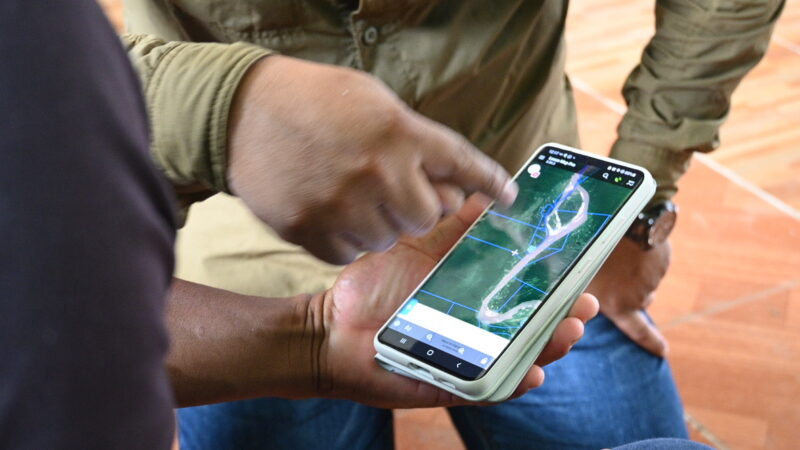 Close-up of someone’s hand holding a cellphone showing a digital map of the rainforest