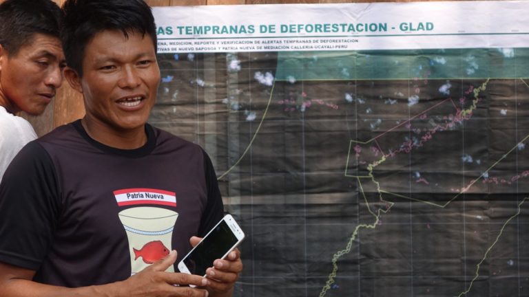 An indigenous man stands in front of a large map showing deforestation alerts in his territory