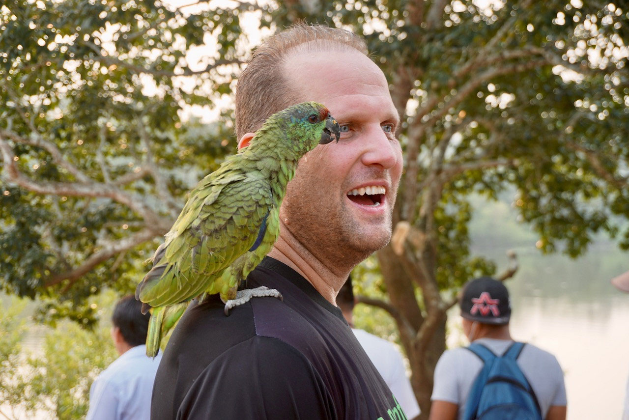 A green parrot sits on the shoulder of Rainforest Foundation US's Peru Country Director, Tom Bewick